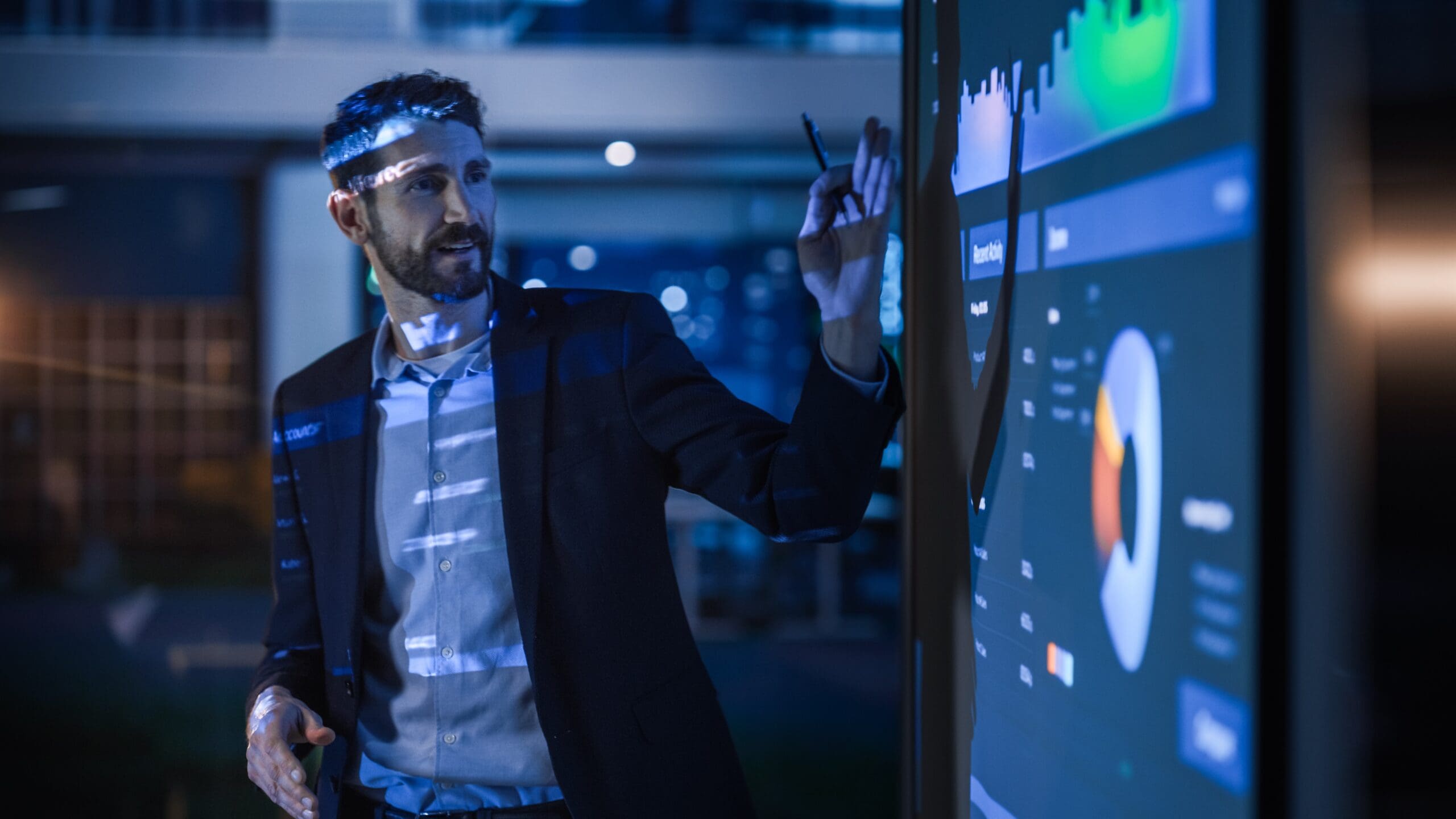 photo of man presenting in front of charts and graphs on a screen