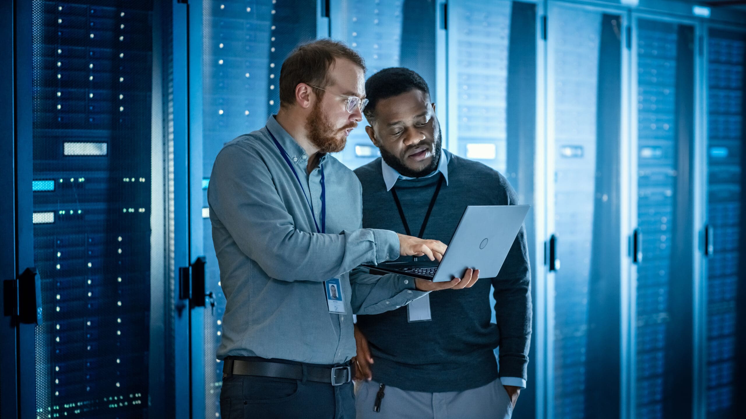 photo of two men looking at a laptop in front of a bank of servers