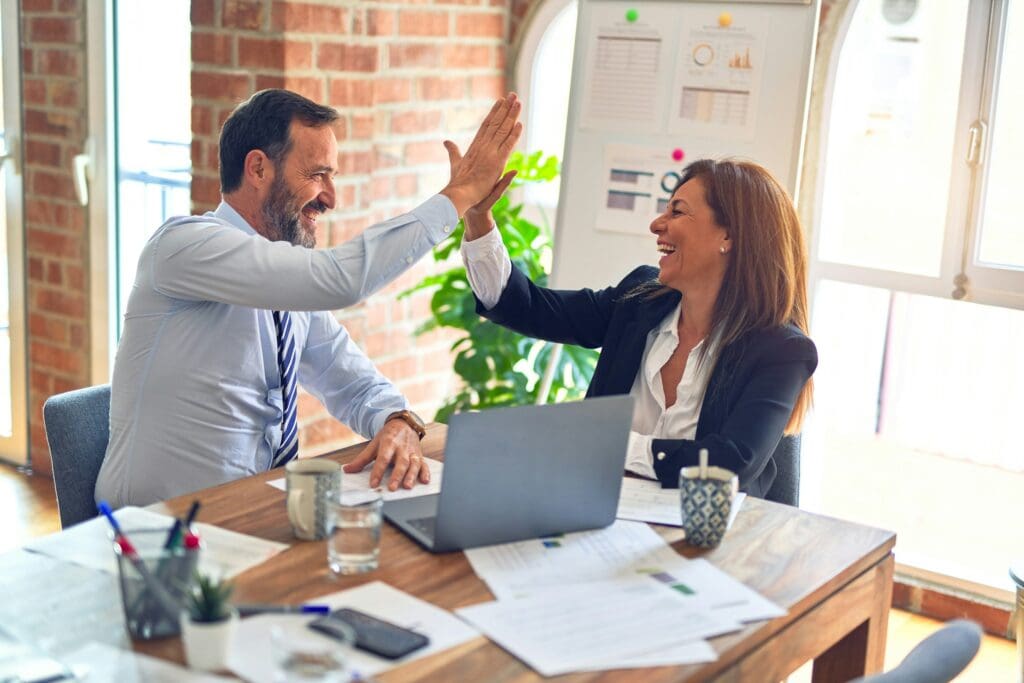 Two team members high-five at their desk as they make a strategic work decision together