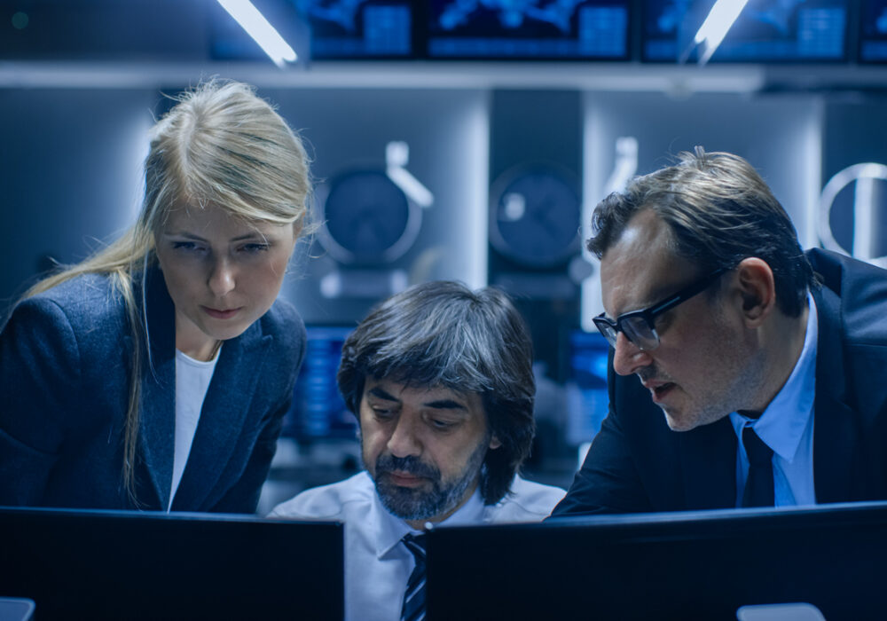 Eine Gruppe von Büroangestellten – männliche und weibliche Mitarbeiter –, die in einem Systemkontrollraum am Computer arbeiten. Analysten einer geheimen Regierungsbehörde, die sich mit Forschung und Cybersicherheit befassen.